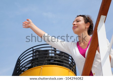 Beautiful woman stands on board of large ship, clings to railing and waves her hand