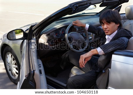Man in a striped suit sits on a driver seat in a open top car