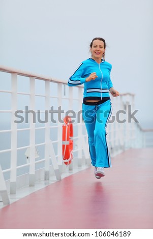 Beautiful woman wearing in blue sports suit runs on cruise liner deck