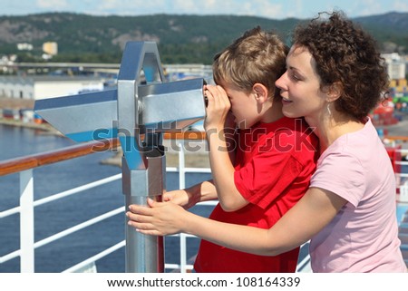Mother and son stand on deck of ship and look through binoculars at beautiful landscape