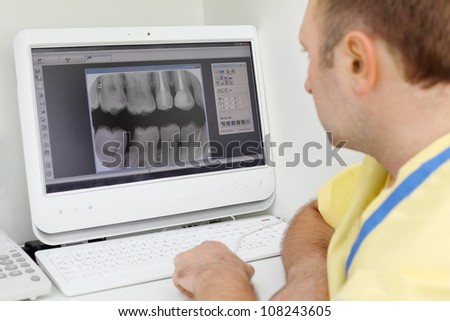 Dentist carefully looks at teeth X-rays at computer monitor in dental clinic. Focus on monitor.
