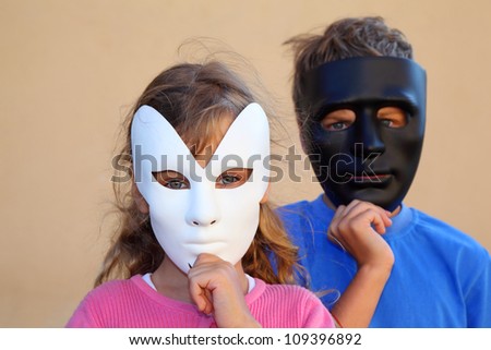 Girl and boy hide faces behind black and white masks and look at camera. Focus on girl.