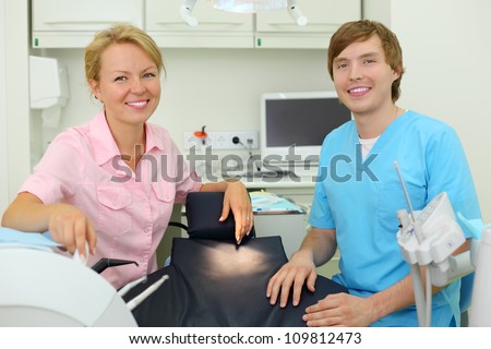 Two young smiling dentists sits in cabinet of dental clinic.