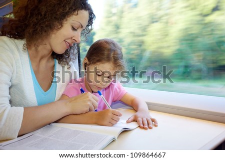 Mother and daughter draw in colour magazine, sitting in armchair of moving speed train