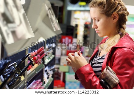 Young woman with braid chooses lipstick in small cosmetics shop.