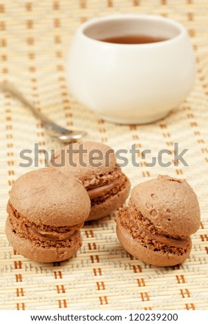 Three cocoa dough sponge drops with cream, cup of tea and teaspoon on cloth-mat