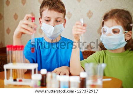 Boy and girl sit at table with chemical reagents and look at test tubes in their hands