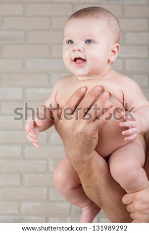 Smiling baby in the arms of his father. Baby looks into the distance.