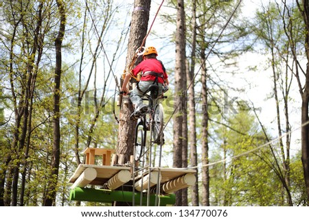 Young climber on a special bike rides on a tightrope on high ropes course.