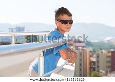 Portrait of a smiling boy stands on the balcony of the hotel and looks into the distance on the background of the mountains.