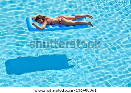 Young woman in red swimsuit bakes lying on inflatable mattress in pool