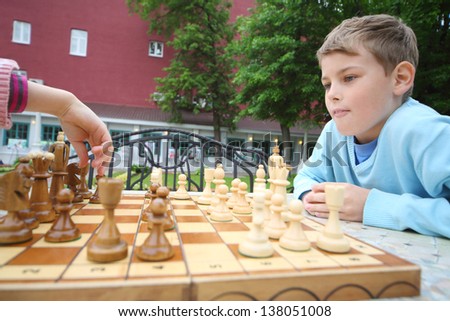 Boy looks like hand of girl moves chess piece on chessboard in park.