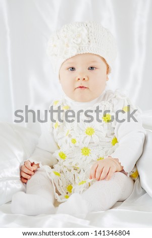Portrait of little girl in white clothes, who sits on white coverlet between pillows
