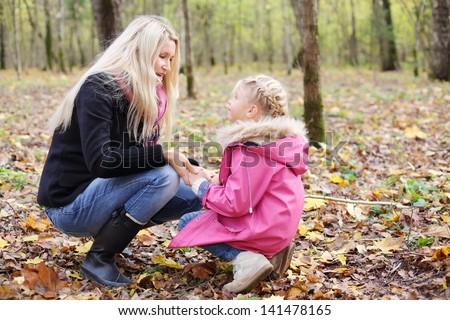 Happy daughter and mother hunker down and look at each other in autumn forest. Focus on mother. Shallow depth of field.