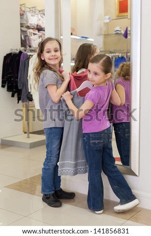 Two little girls near a mirror try on clothes in a store children clothes, focus on left girl
