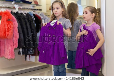 Two little cute girls near a mirror try on clothes in a store children clothes