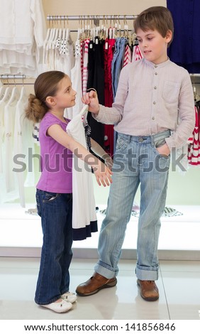 The boy helps girl to choose clothes in shop of childrens clothing