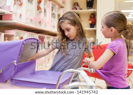 Two girls in a toy store with dolls look into the buggy, focus on left girl