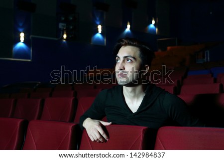 Young beautiful man watches movie and smiles in movie theater.