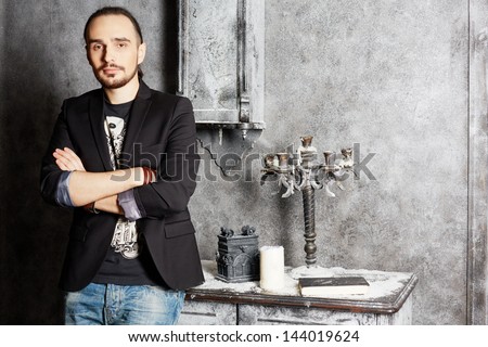Young man stands with arms folded leaning on old vintage table