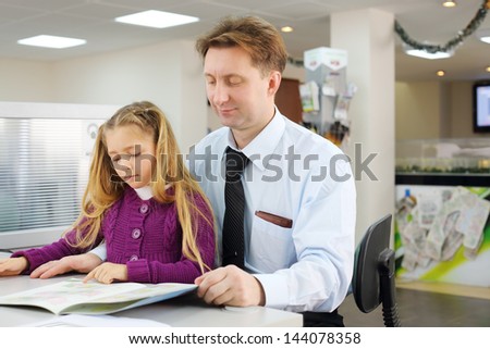 Happy girl and her father choose apartment by floor plan booklet in office.