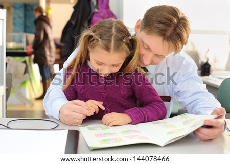 Happy girl and her father look at floor plan booklet in office. They choose apartment.