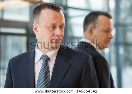 A businessman in a suit and tie stands near a mirror