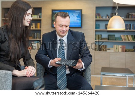 A girl with a man in business suits sitting on chairs with notebook, focus on a man.