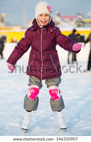 Smiling little girl in knee pads skating at the rink