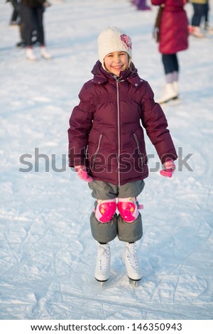 Smiling little girl in knee pads skating at the rink in winter