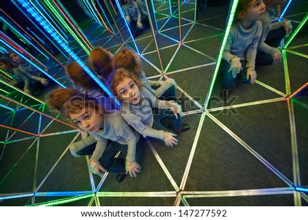 Little girl sits at crossing in mirror labyrinth illuminated with color lights