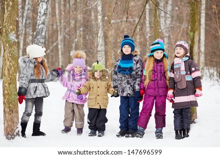 Six children  stand holding hands in winter park, four older and two younger