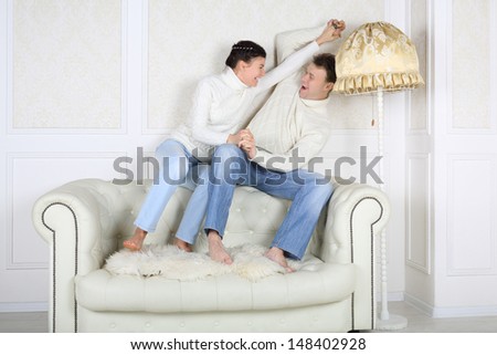 Smiling husband and wife sits on back of white sofa and fight at home.