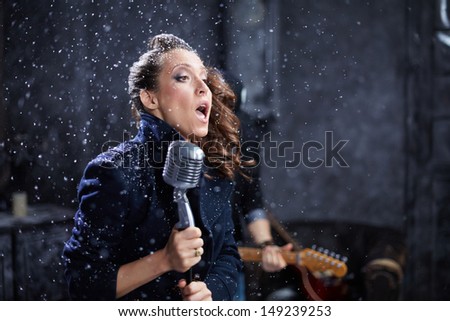 Young female vocalist sings into microphone during shooting video clip