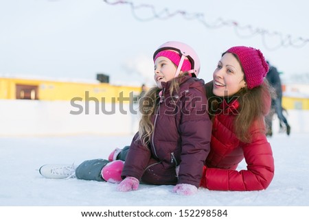 Happy mother and daughter sitting on the outdoor skating rink in winter
