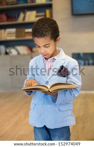 Little mulatto boy in a modern striped jacket read a book in library