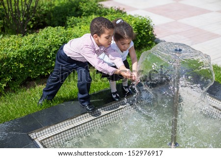 Brother and sister mulatto draw water from the fountain in the park