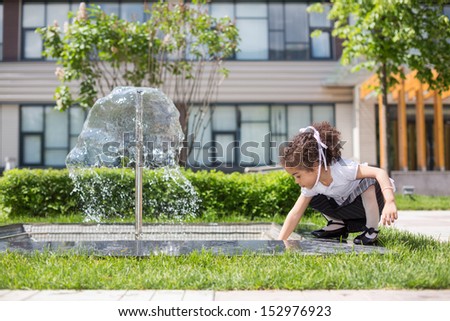 Girl mulatto draw water from the fountain in the park
