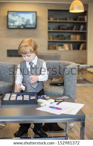 Little boy in business clothes playing with a mineral samples in room with books and screen