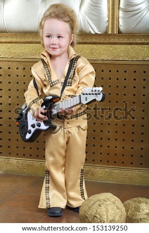 A small boy in pop retro suit playing the guitar