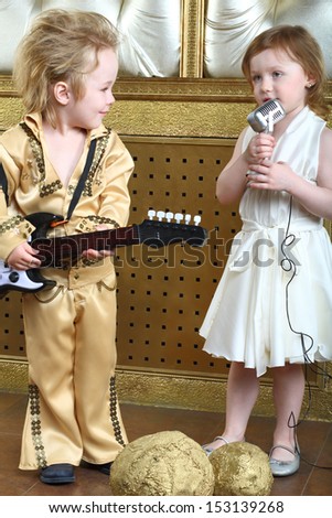 A little girl in white dress sings a song and pop musician plays guitar