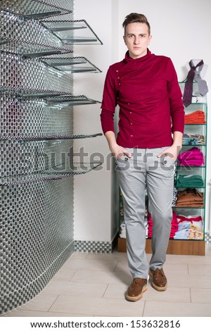 The man in gray pants and a red sweater in a clothing store with shelfs