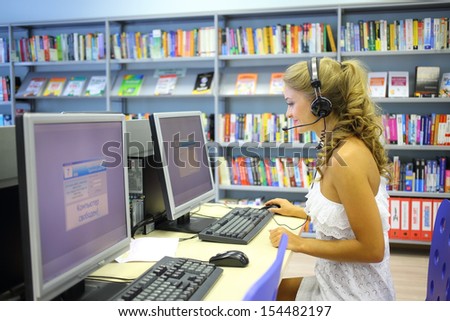 A happy beautiful woman wearing headphones looking at a computer in the library