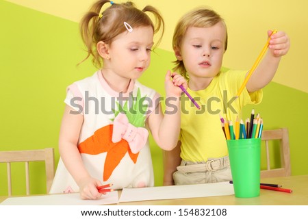 Little boy and girl picking a colored crayon from the pencil cup