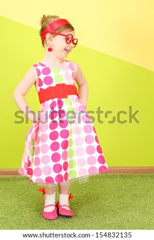Mod little girl in a bright dress and large red glasses, hands on belt