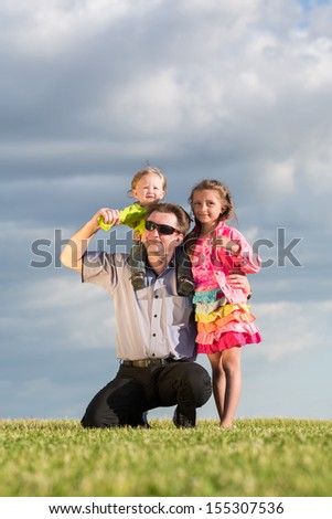 Happy family of three on green grass and blue sky, father sat down and put  son on the neck.