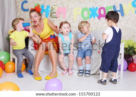 Four little kids with juice and entertainer sit on sofa at funny children party.