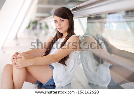 Smiling girl in white blouse and shorts sits near long travelator.