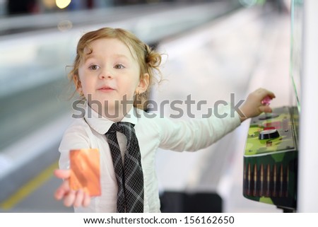 Little red hair girl in white shirt and tie plays on game machine and shows credit card.