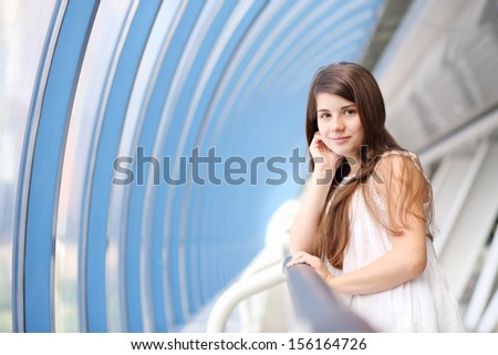 Smiling girl in white blouse stands in long light gallery and looks at camera.